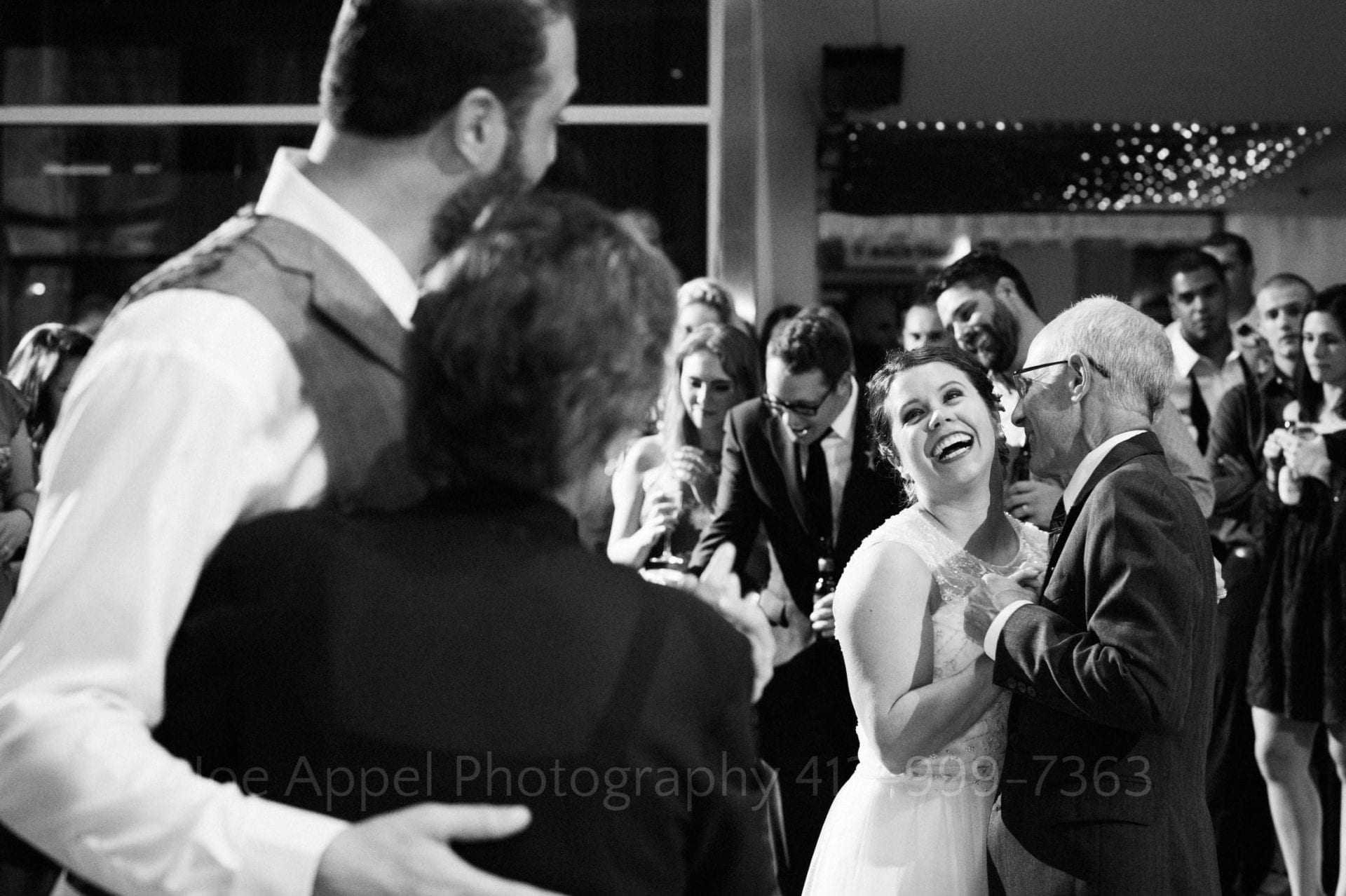A bride dancing with her father looks over at her groom who is dancing with his mother and smiles.