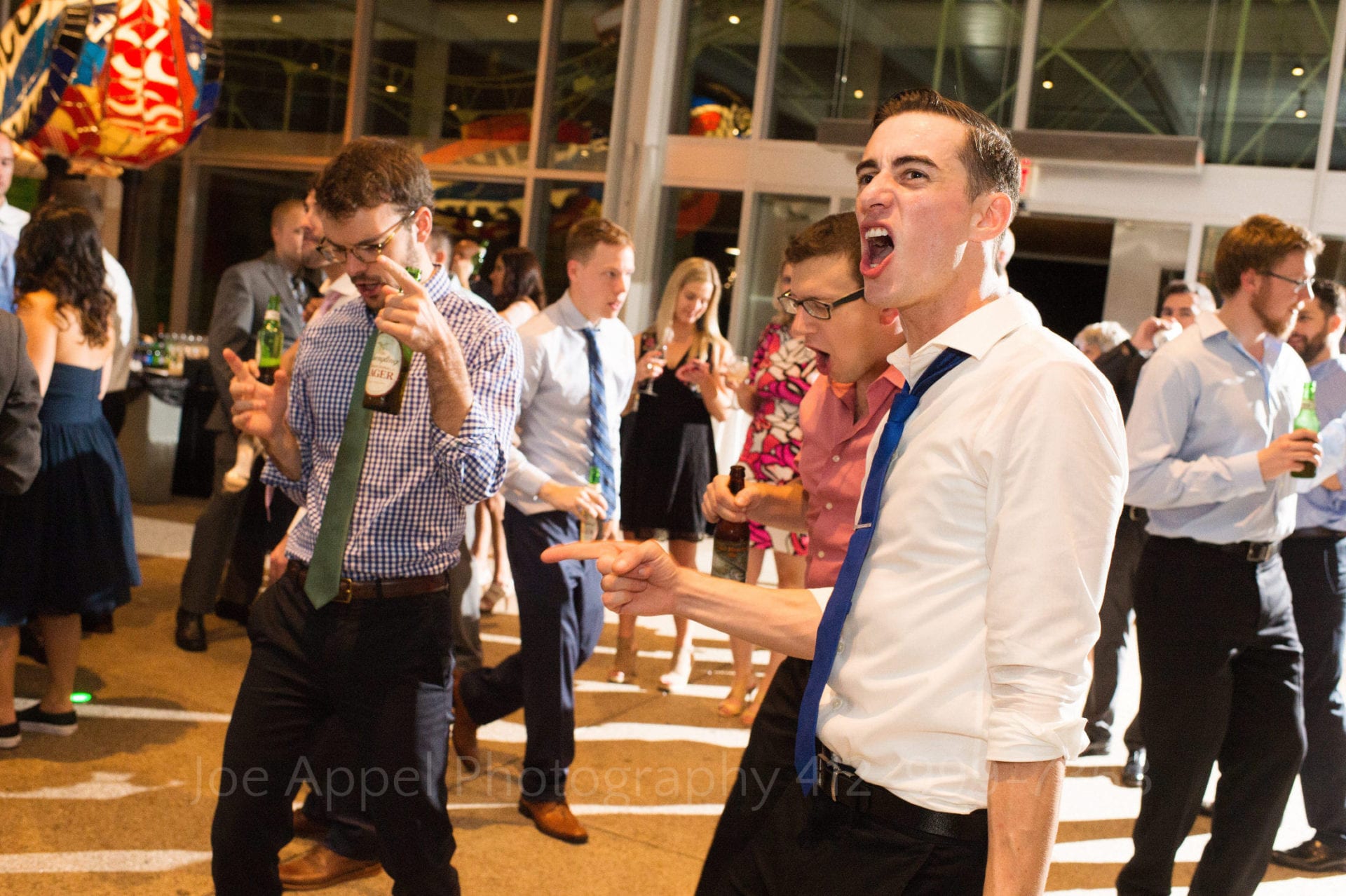 Men in shirts and ties dance during a wedding reception.