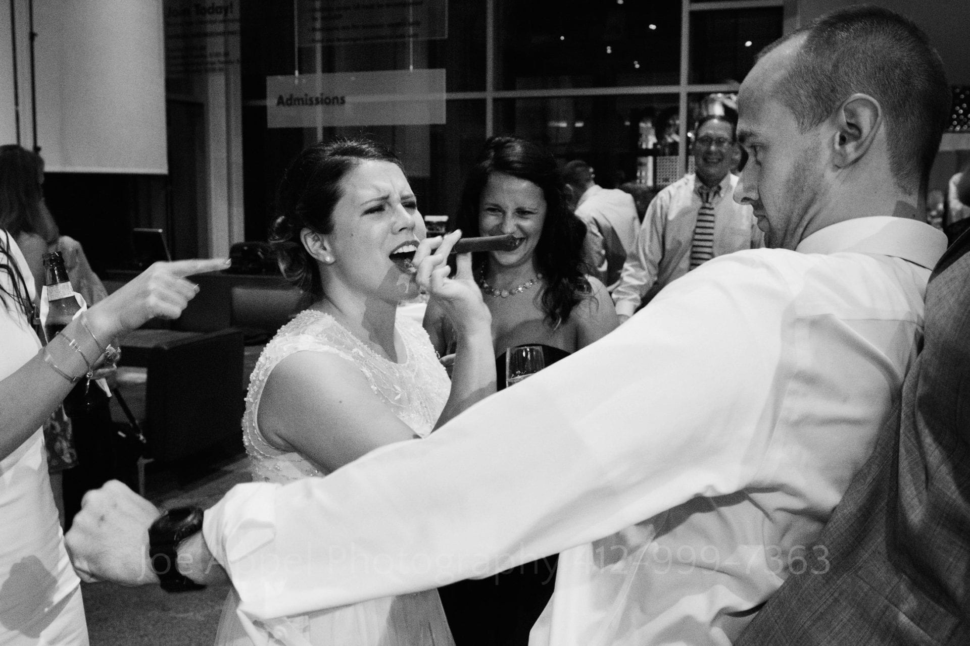 A bride holding a cigar in her mouth dances with a man in a white shirt.