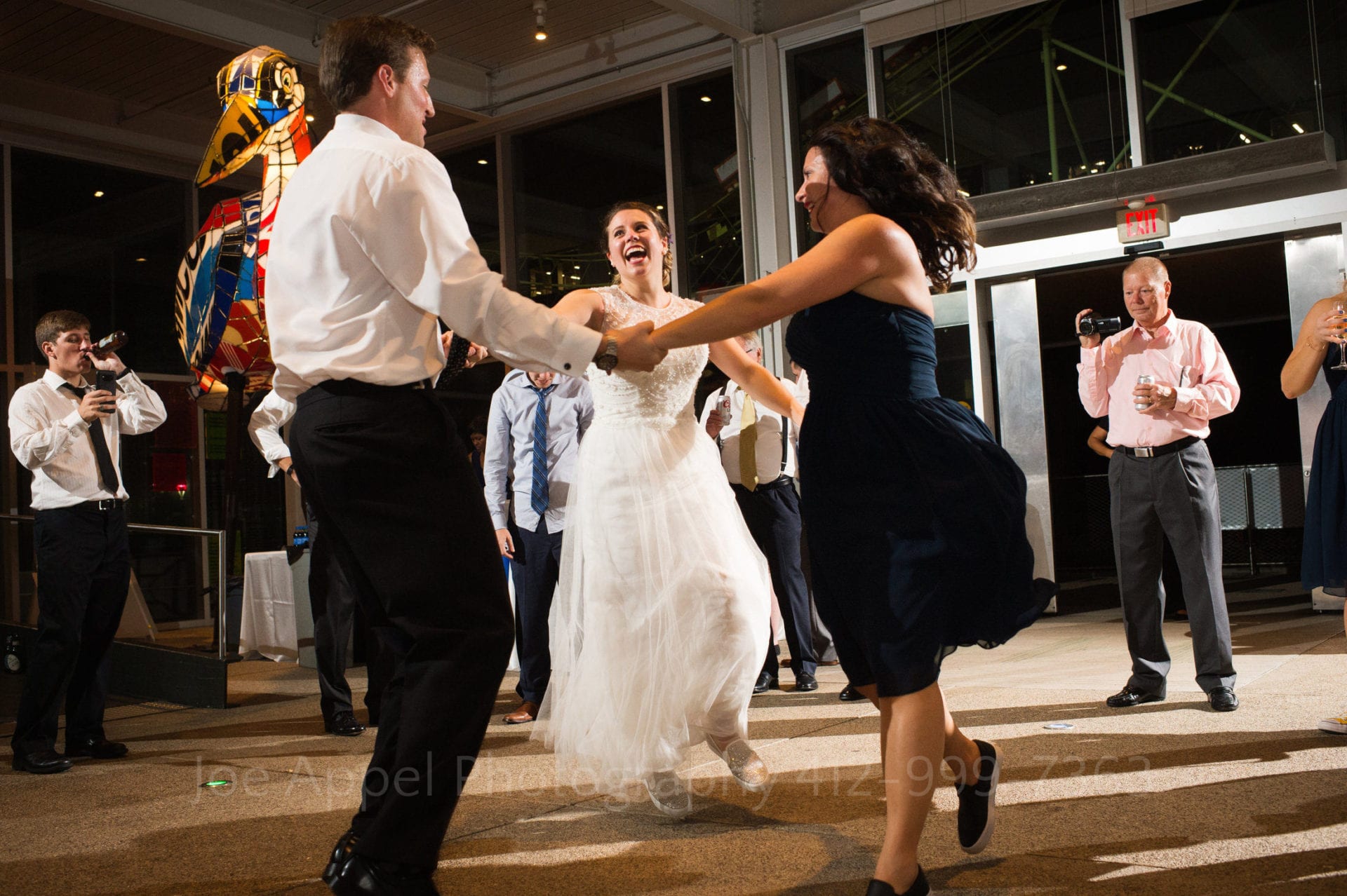 A bride holds hands and dances in a circle with a man and a woman during her Children's Museum of Pittsburgh wedding.