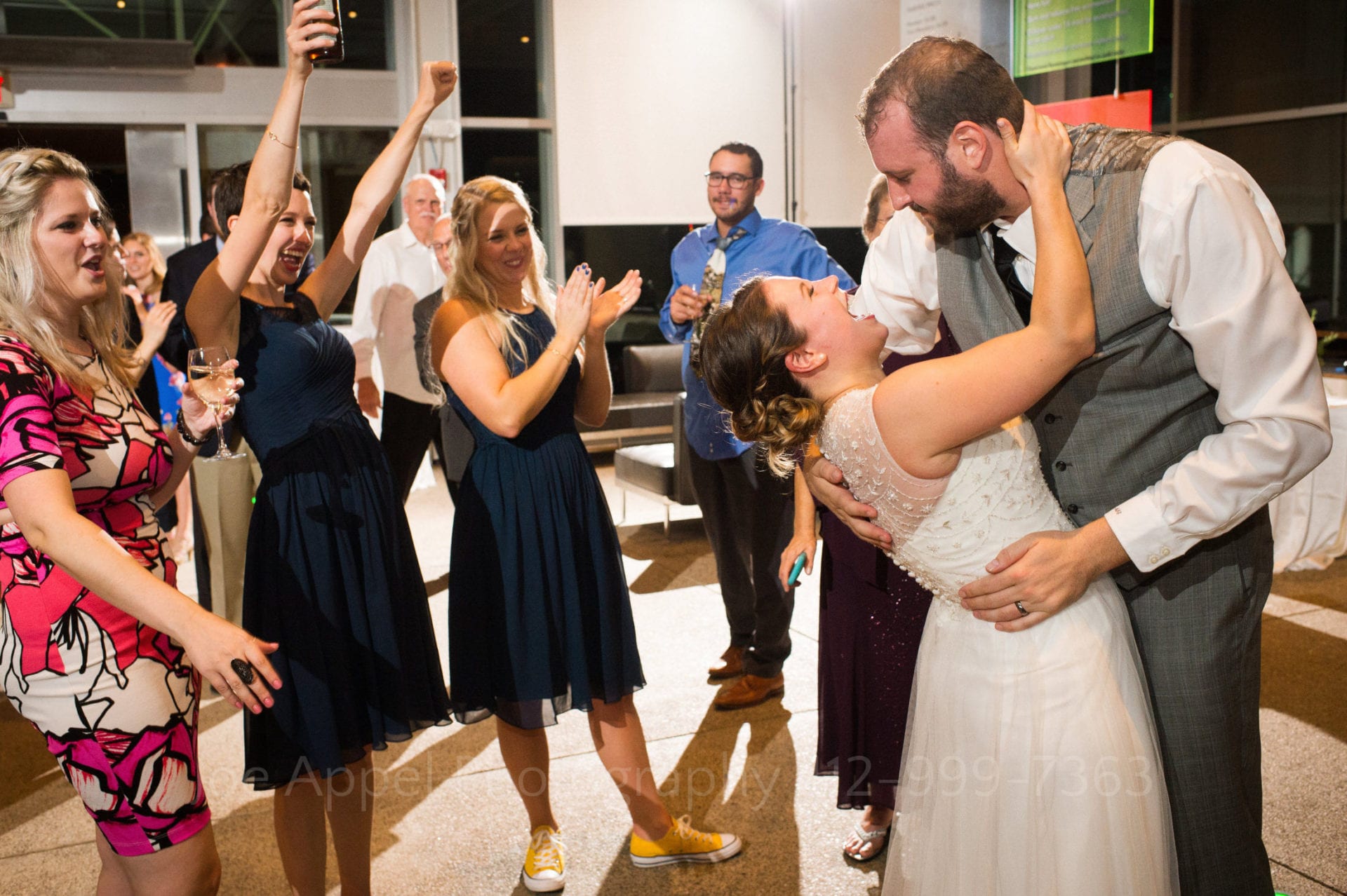 A groom dips his bride who laughs while three women cheer at the end of their Children's Museum of Pittsburgh wedding.