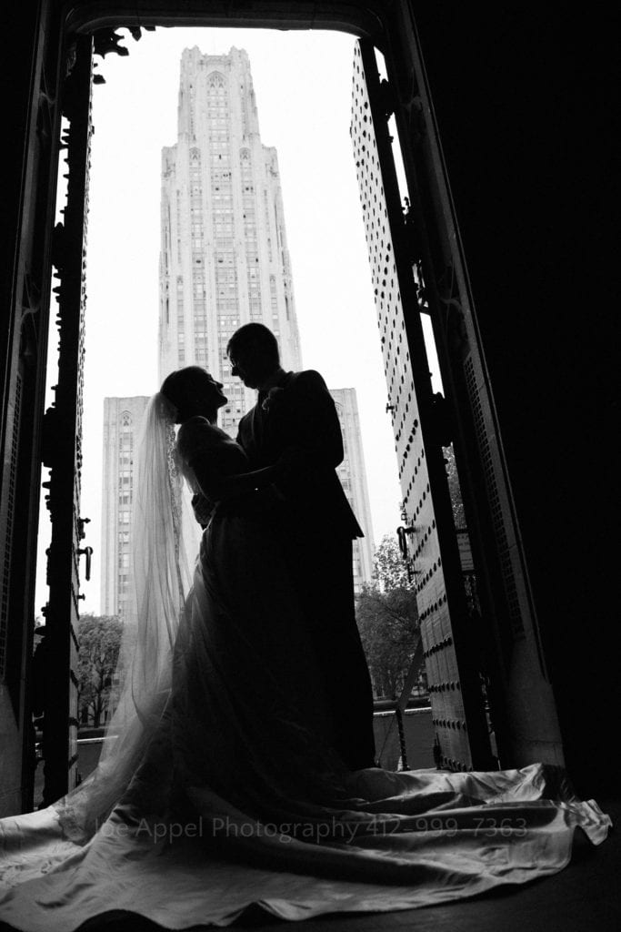 Silhouette of a bride and groom embracing in the doorway after their Heinz Chapel wedding. The University of Pittsburgh's Cathedral of Learning is in the background.