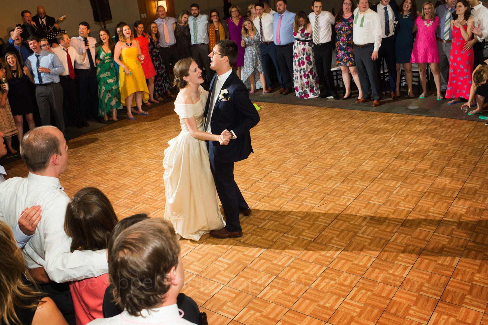 A bride and groom dance in the middle of an empty dance floor as their guests surround the edges and serenade them at the end of their Heinz History Center wedding.
