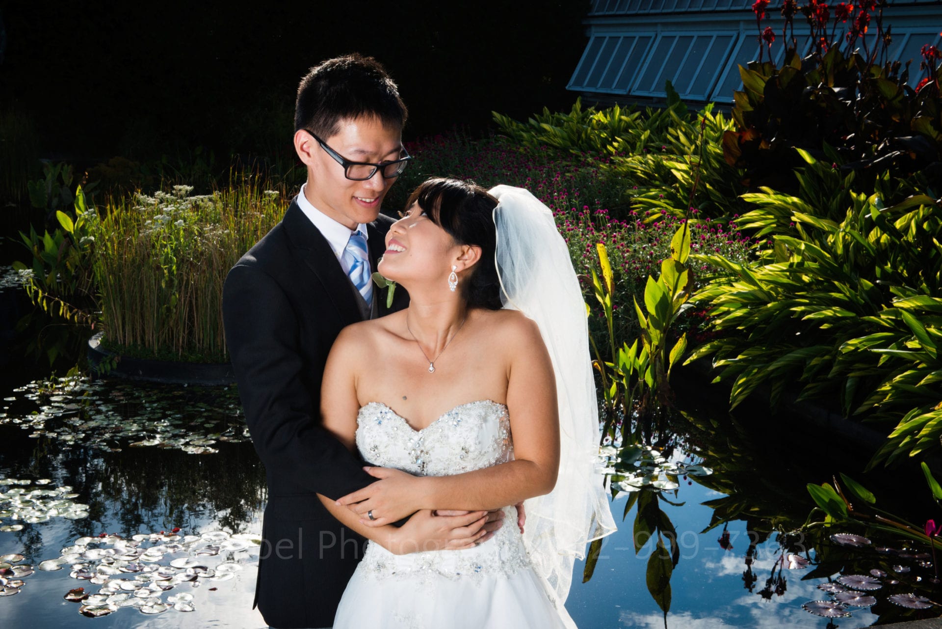 a bride and groom smile and pose by a pond after their Phipps Conservatory Wedding.