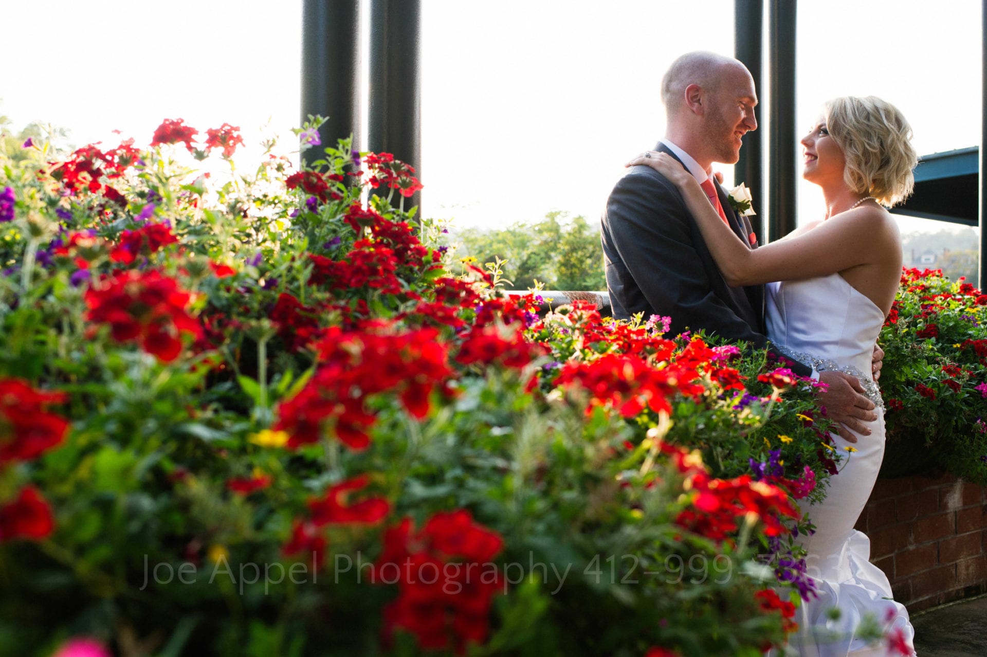 A couple stands at the right side of the frame behind a planter filled with red flowers at the entrance to the Pittsburgh Zoo and PPG Aquarium.
