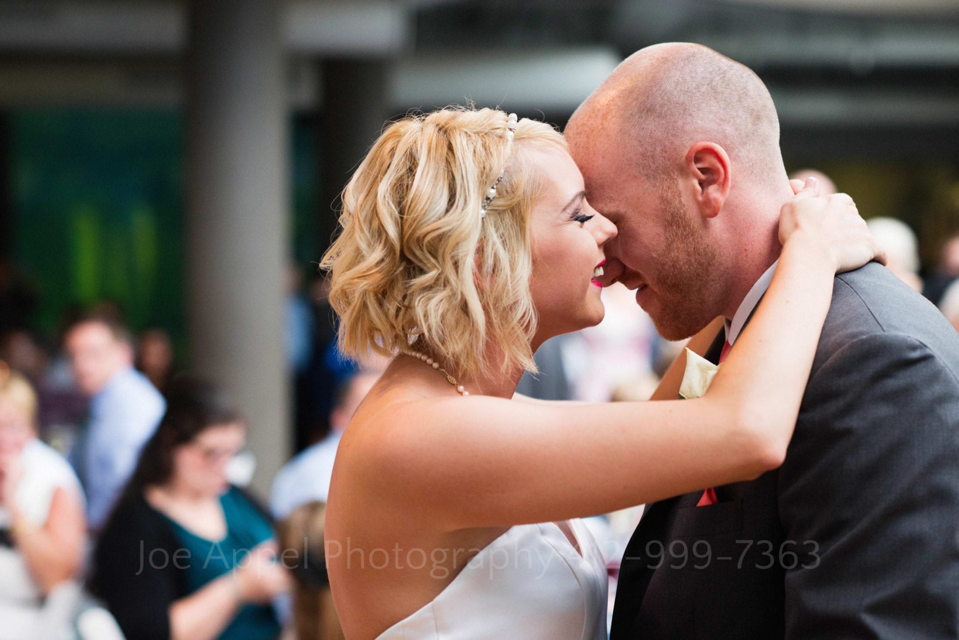 A blonde bride smiles as she has her hands around the neck of her groom.
