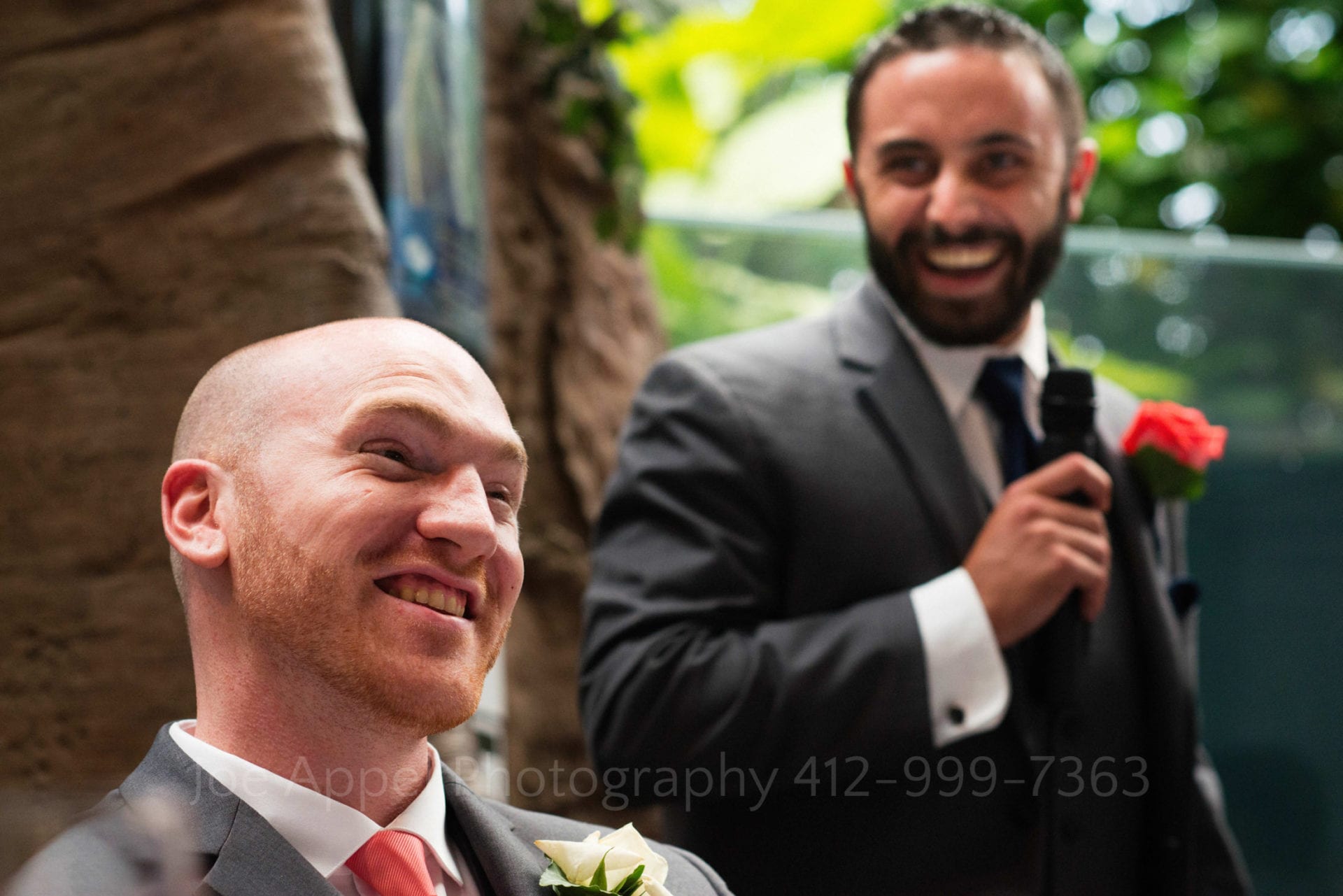A groom smiles as his best man stands behind him and gives a toast at his PPG Aquarium Wedding.