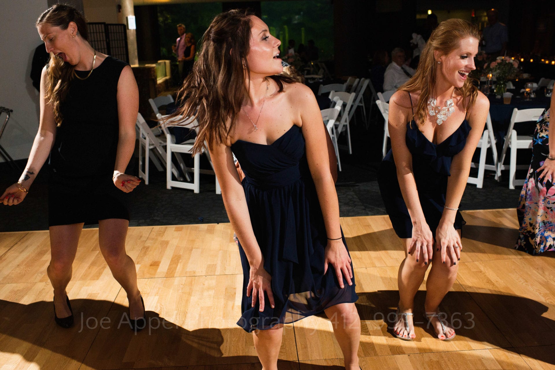 Three women dance with their hands on their knees during a PPG Aquarium wedding reception.
