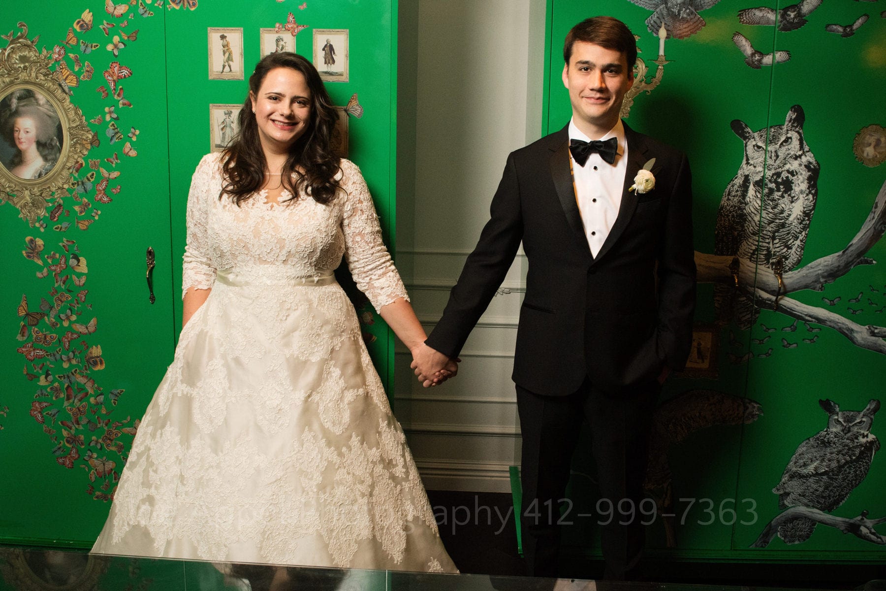 a bride and groom hold hands in front of the large green cabinet with images of owls and french revolutionary figures at the Hotel Monaco Pittsburgh wedding.