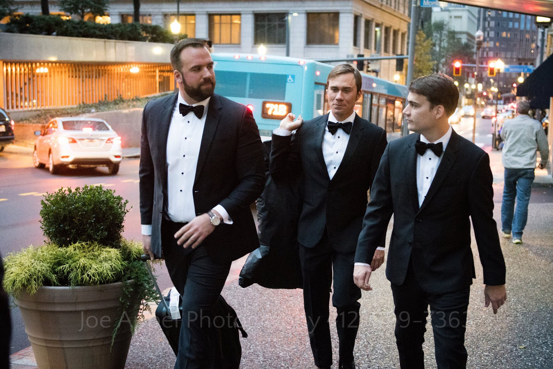 a groom and two groomsmen walk on the street in downtown pittsburgh with the 71B bus in the background to a hotel monaco pittsburgh wedding