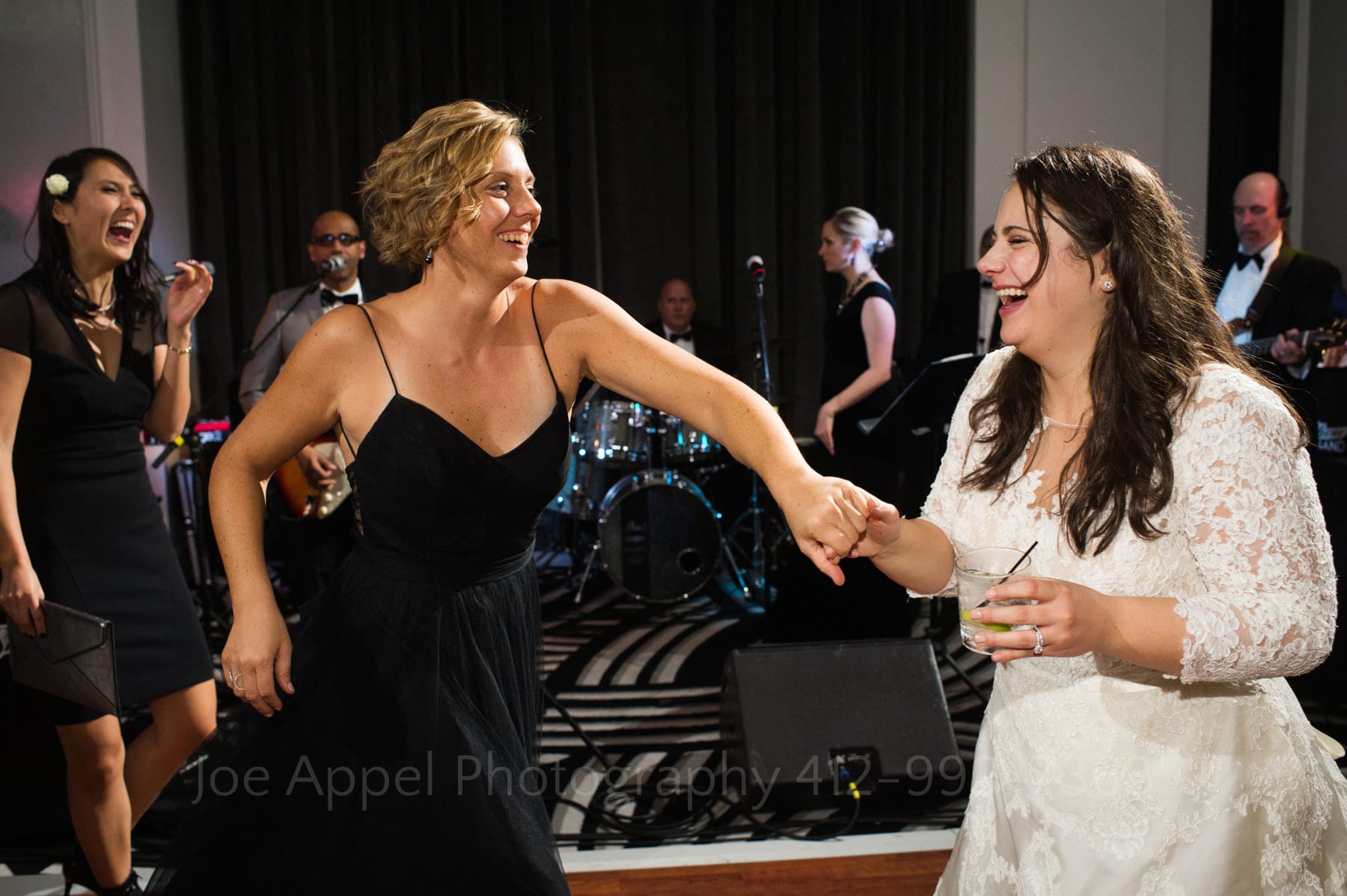 a bride drinks and dances with her maid of honor. They're both sweating and laughing.