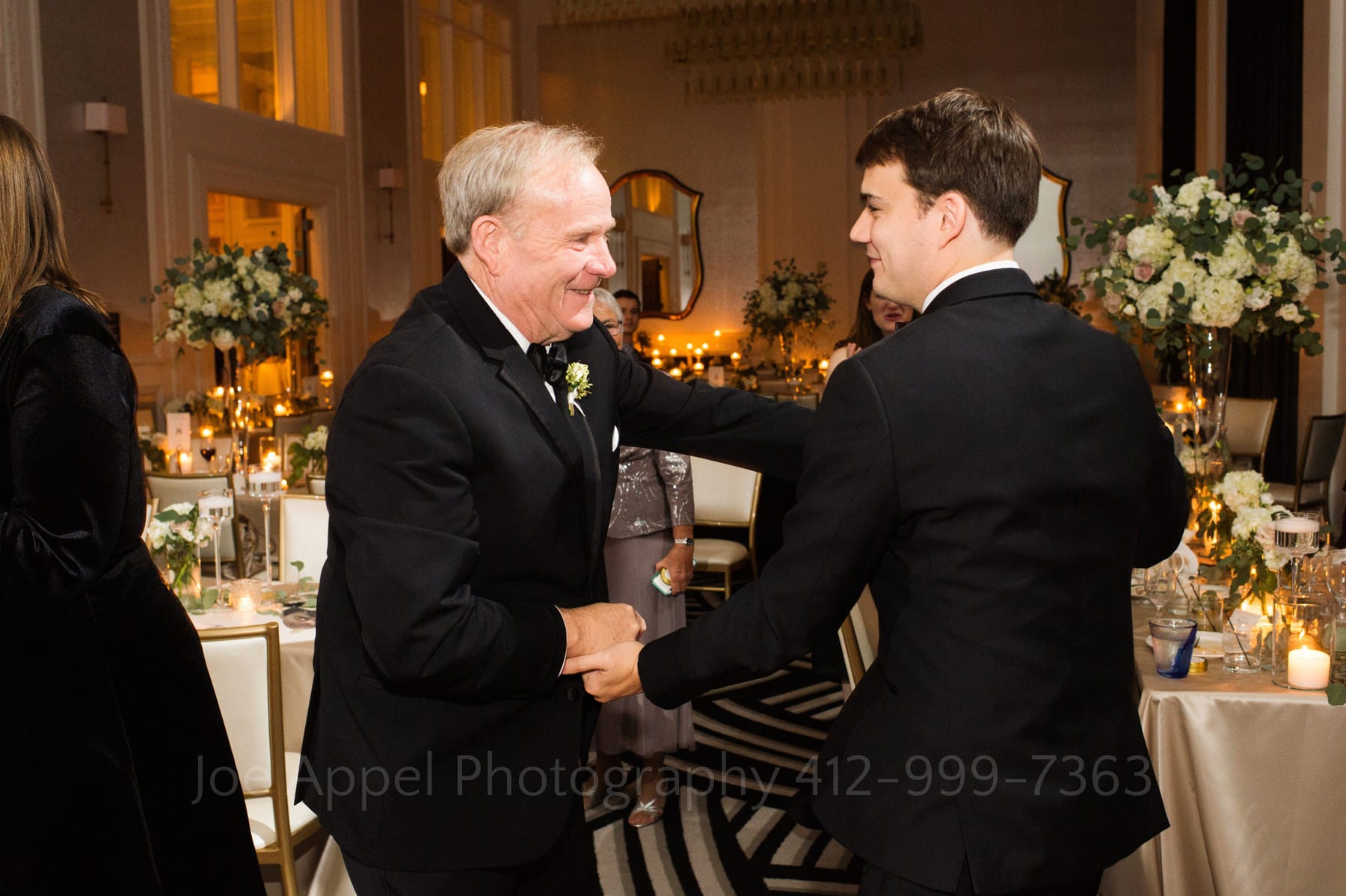 a groom dances with his father, they're both wearing black tuxedos.