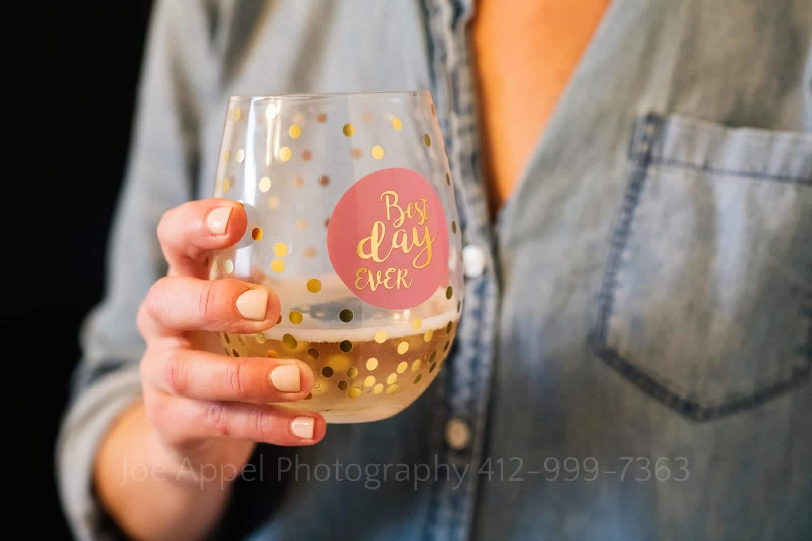 Detail photo of a woman in a blue shirt with ecru-colored nail polish holding a tumbler with the phrase Best Day Ever before her St Francis Hall Washington DC wedding