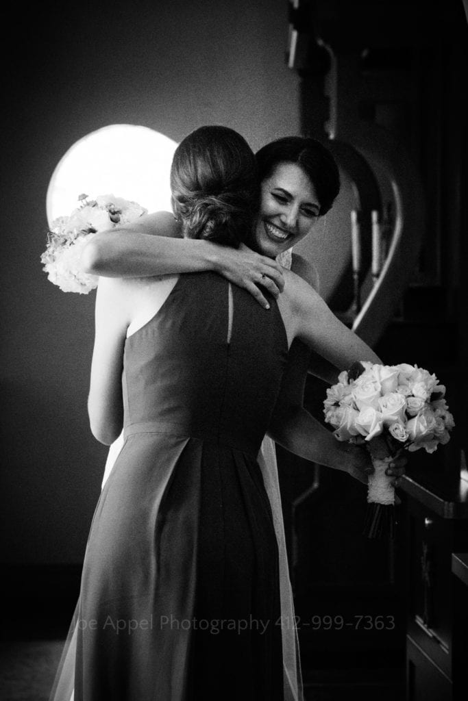 A bride smiles as she embraces her matron of honor in the back of St. Mary's Armenian Apostolic Church in Washington DC.