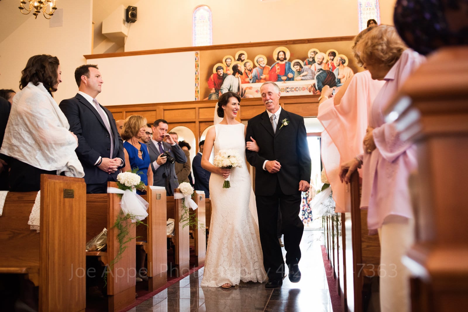 A bride smiles as she looks at her father while they walk down the aisle of St. Mary's Armenian Apostolic Church in Washington DC.