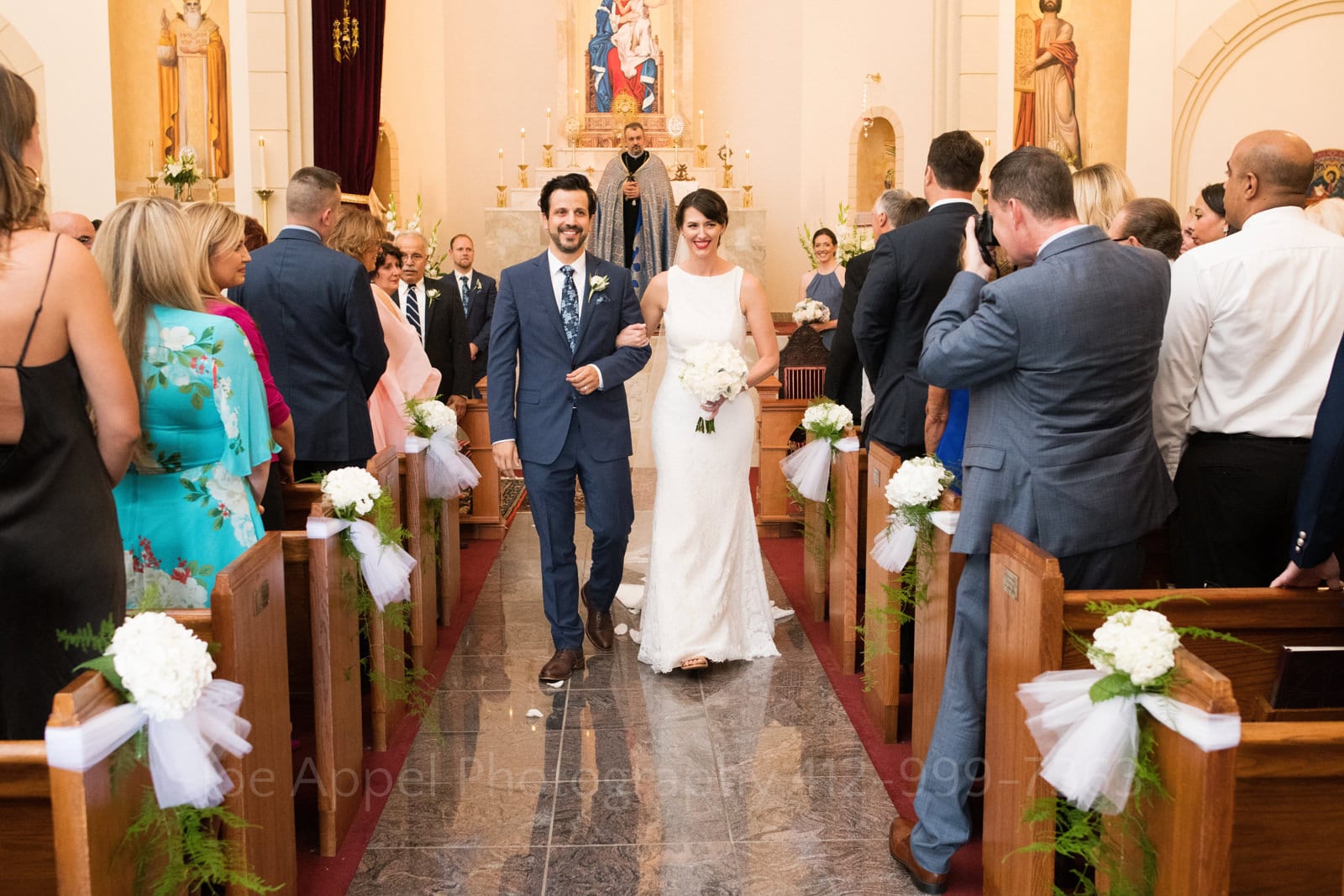 A smiling bride and groom walk down the aisle at the end of their wedding ceremony at St. Mary's Armenian Apostolic Church in Washington DC.