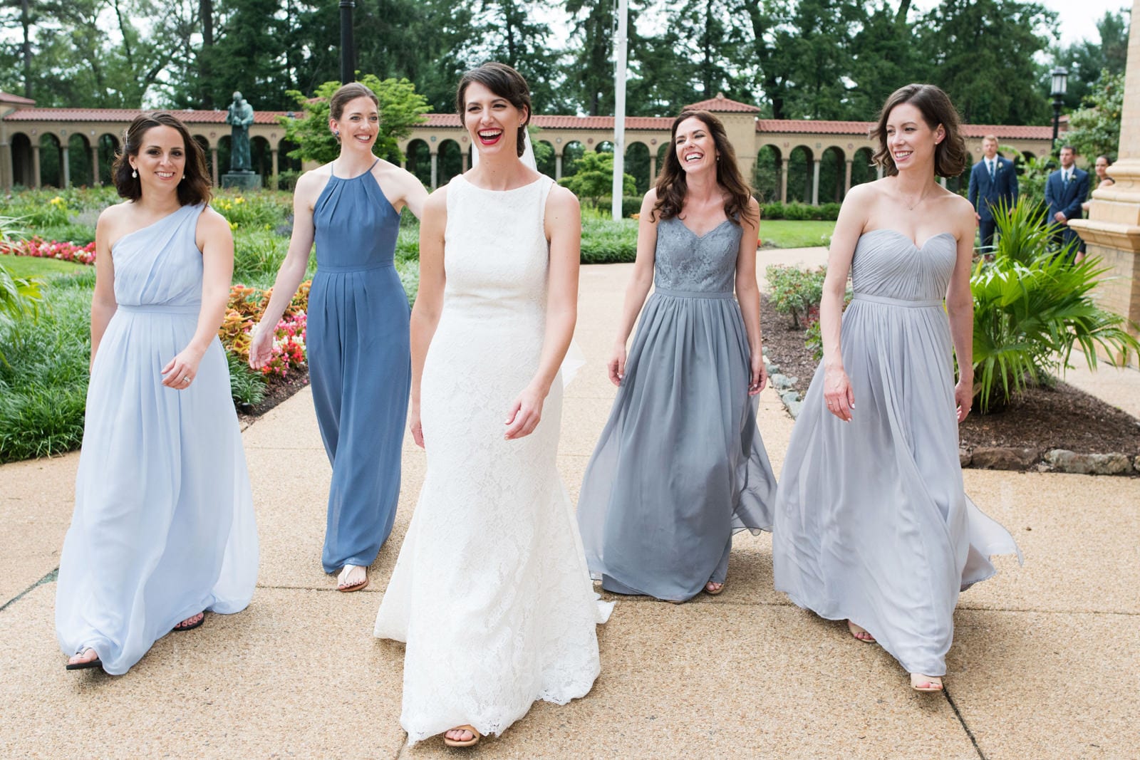 A bride smiles as she and her bridesmaids in blue dresses walk together during her St Francis Hall Washington DC wedding.