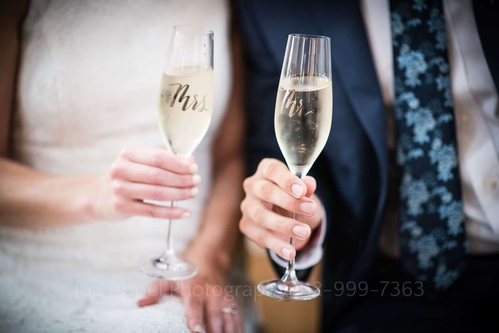 Detail of the hands of a bride and groom holding champagne flutes monogrammed with Mrs and Mr on them at their St Francis Hall Washington DC wedding.