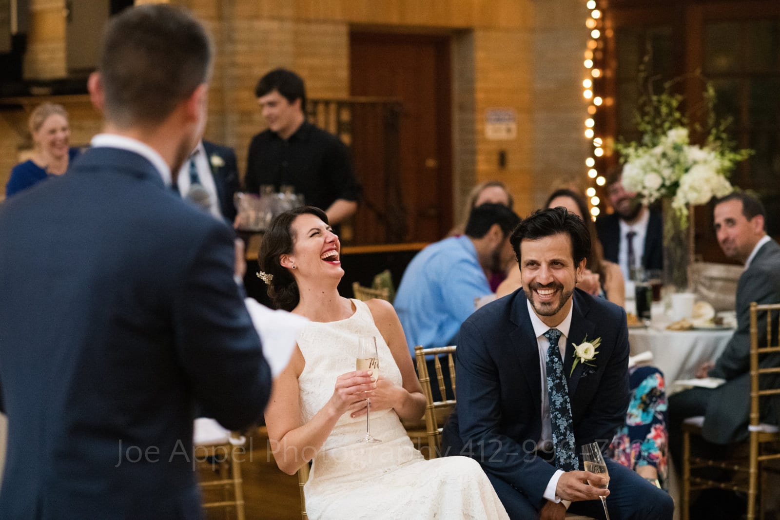 A bride and groom laugh as they listen to a groomsman deliver a toast during their St Francis Hall Washington DC wedding.