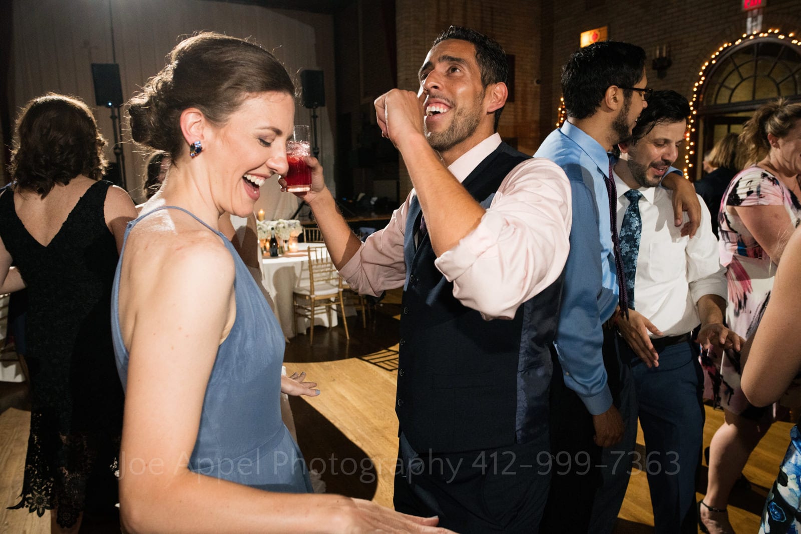 A woman in a blue dress dances with a man wearing shirt sleeves and a vest holding a red drink during a St Francis Hall Washington DC wedding.