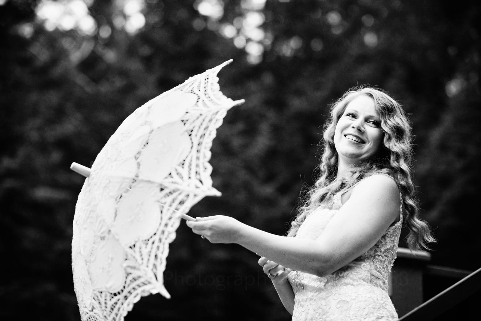 A bride wearing a white lace dress with long curly blonde hair pops open a parasol before her Fall Wedding at Seven Springs.