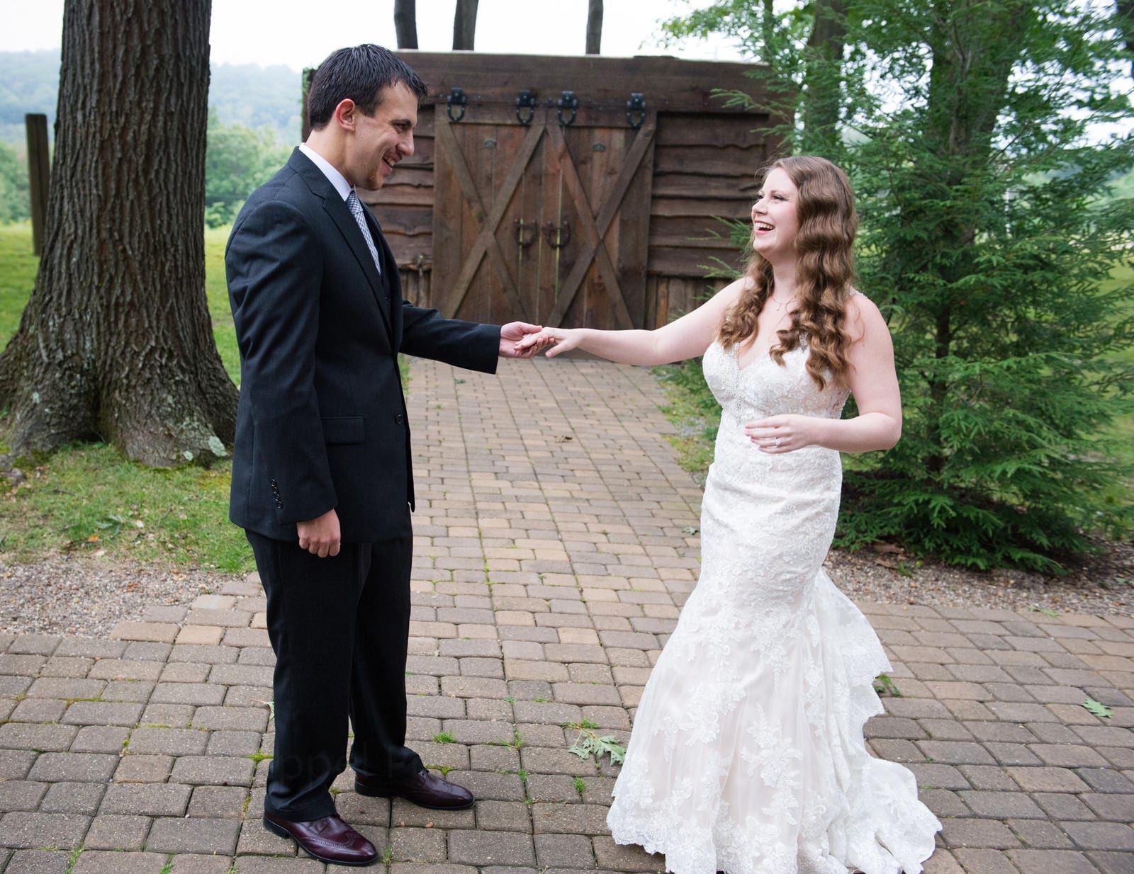 A bride and groom hold hands as the groom sees his bride for the first time. They're standing on a brick patio in front of a small wooden building during their Fall Wedding at Seven Springs.