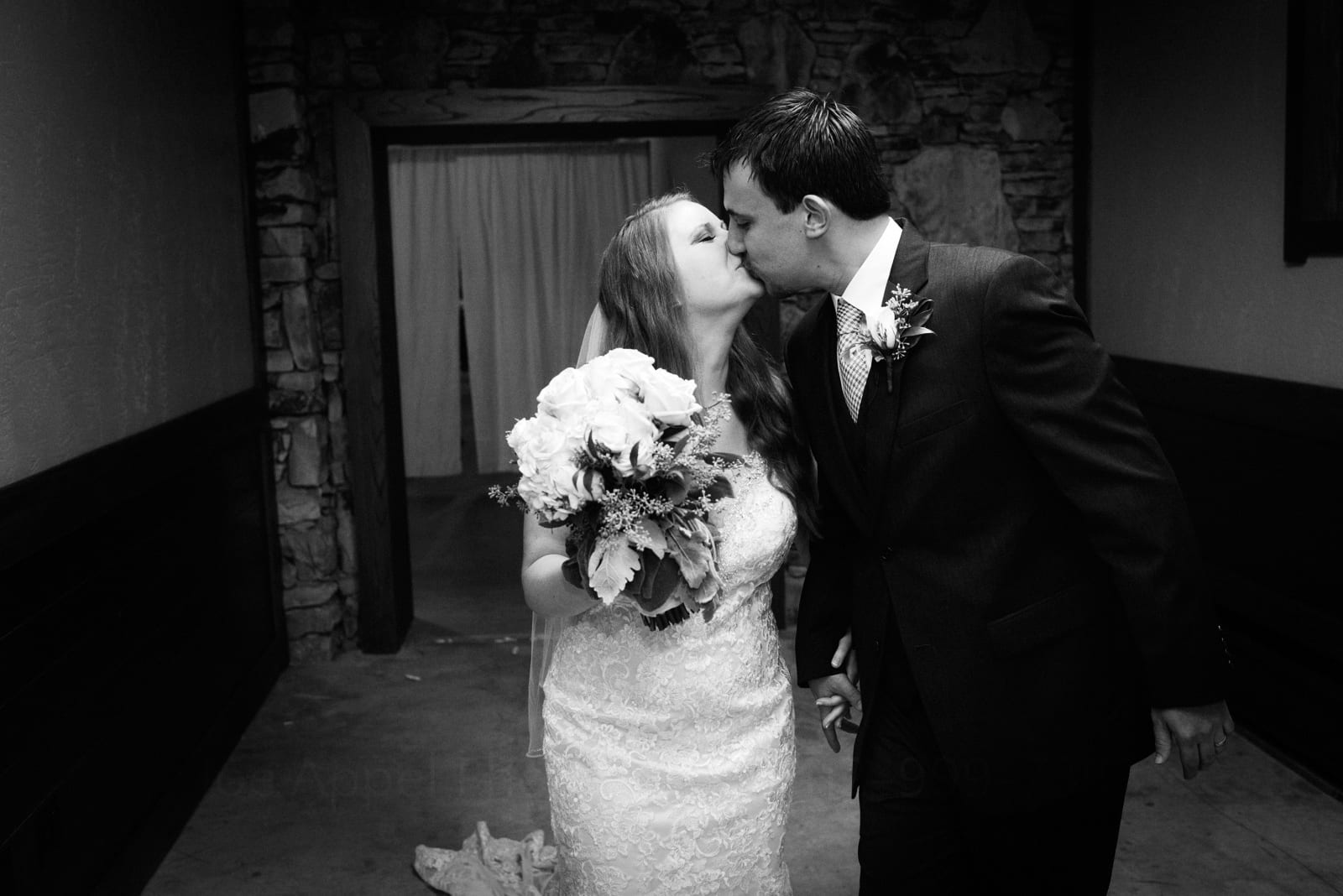 A bride and groom walk down a hallway while kissing each other on the lips during their Fall Wedding at Seven Springs.