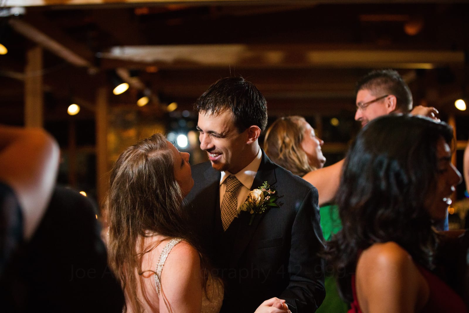 A bride and groom smile at each other as they dance surrounded by other couples during their Fall Wedding at Seven Springs.