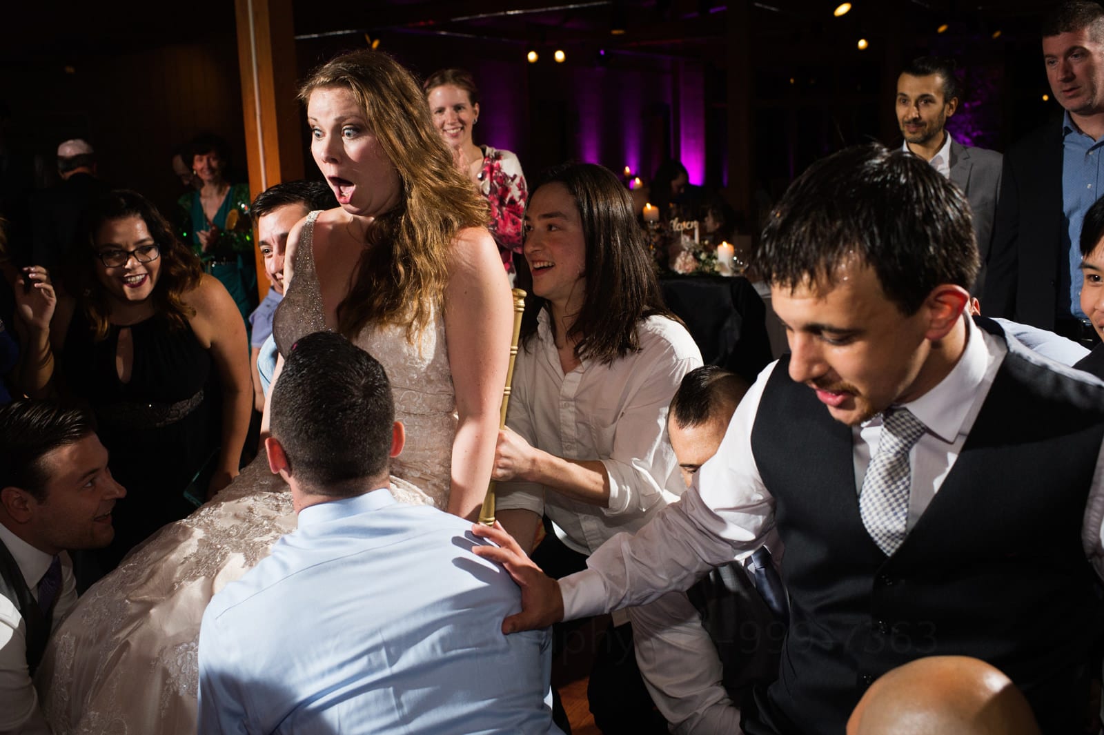 A bride makes a shocked expression as she and her groom are lifted up on chairs during their fall wedding at Seven Springs.