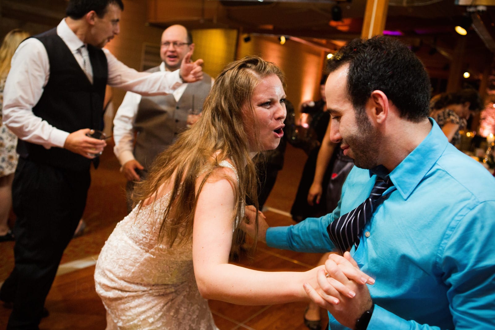 A bride makes a funny expression as she dances with a male guest in a bright blue shirt during her fall wedding at Seven Springs.