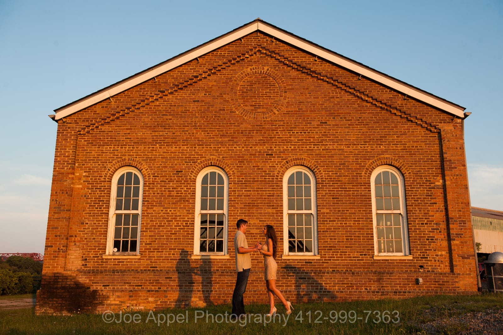 A couple stands face to face in front of an old brick building during their Pump House Engagement Photography session.