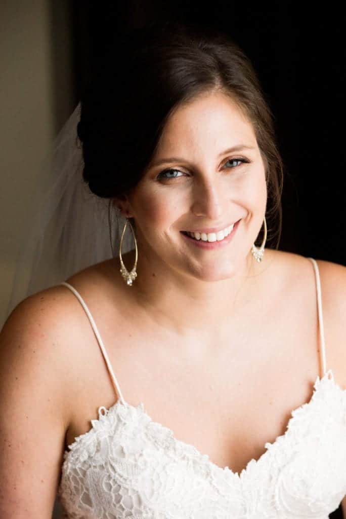 A smiling bride with hoop earrings and a spaghetti strap gown before her Wedding Photography at Fairmont Hotel Pittsburgh.