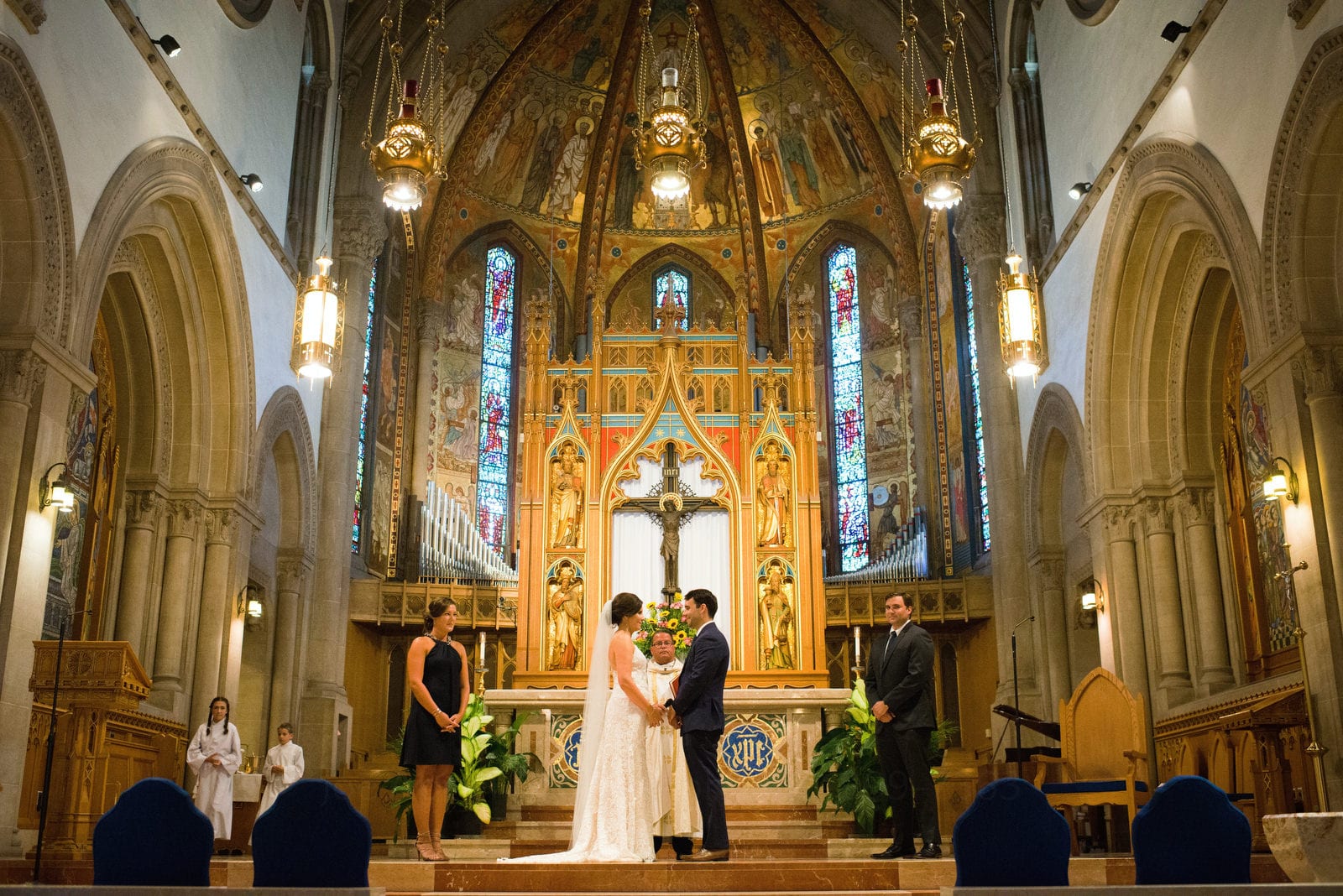 A gold-gilded altar with a bride and groom standing hand in hand in front of a priest Wedding Photography at Fairmont Hotel Pittsburgh.