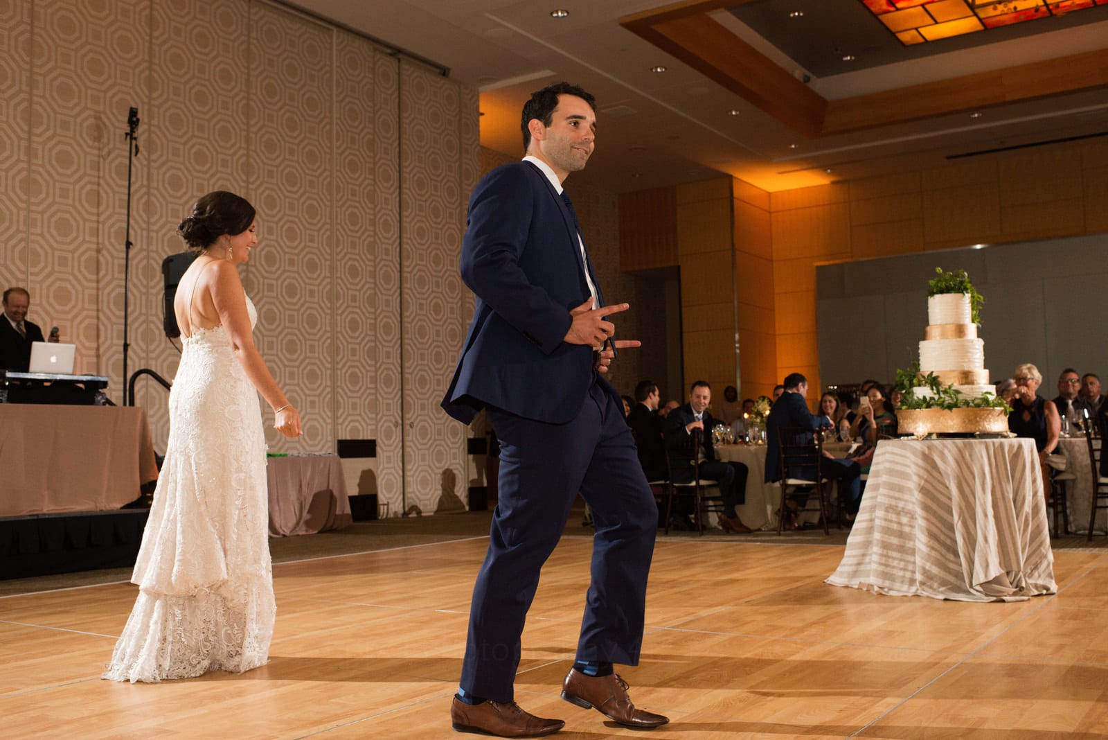 A groom in a blue suit dances with his hands like six-shooters while his bride laughs during their Wedding Photography at Fairmont Hotel Pittsburgh.