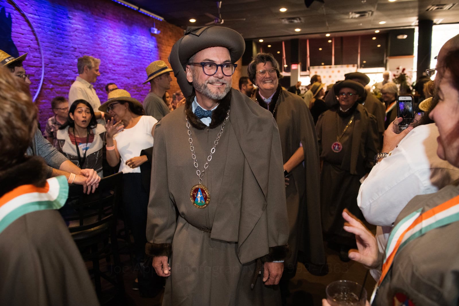 A smiling man wears a brown robe and a hat shaped like a wheel of cheese during a ceremony Pittsburgh editorial event photographer.