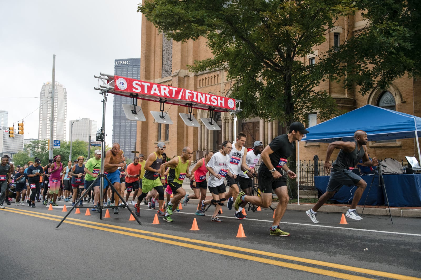 A group of runners take off through a starting gate on a street in the hill district of Pittsburgh. Pittsburgh editorial event photographer.