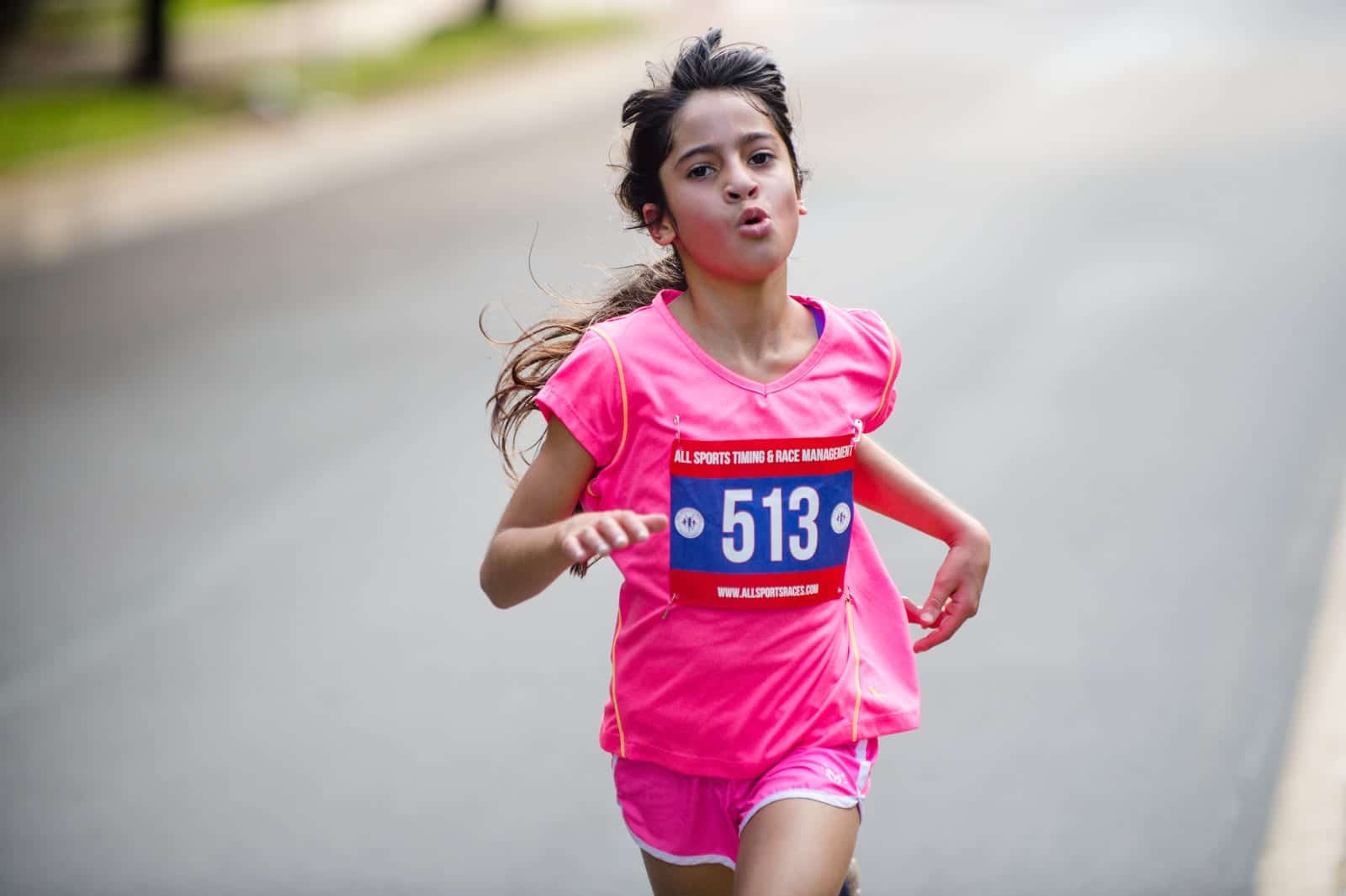 A young girl wearing a pink t-shirt and shorts runs very fast during a 5K race. Pittsburgh editorial event photographer.