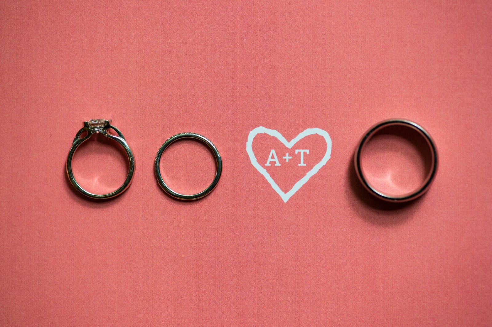 A heart with initials A+T inside of it is printed on salmon-colored cardstock. A couples' wedding bands are arranged next to it during their Hyeholde Wedding Pittsburgh.