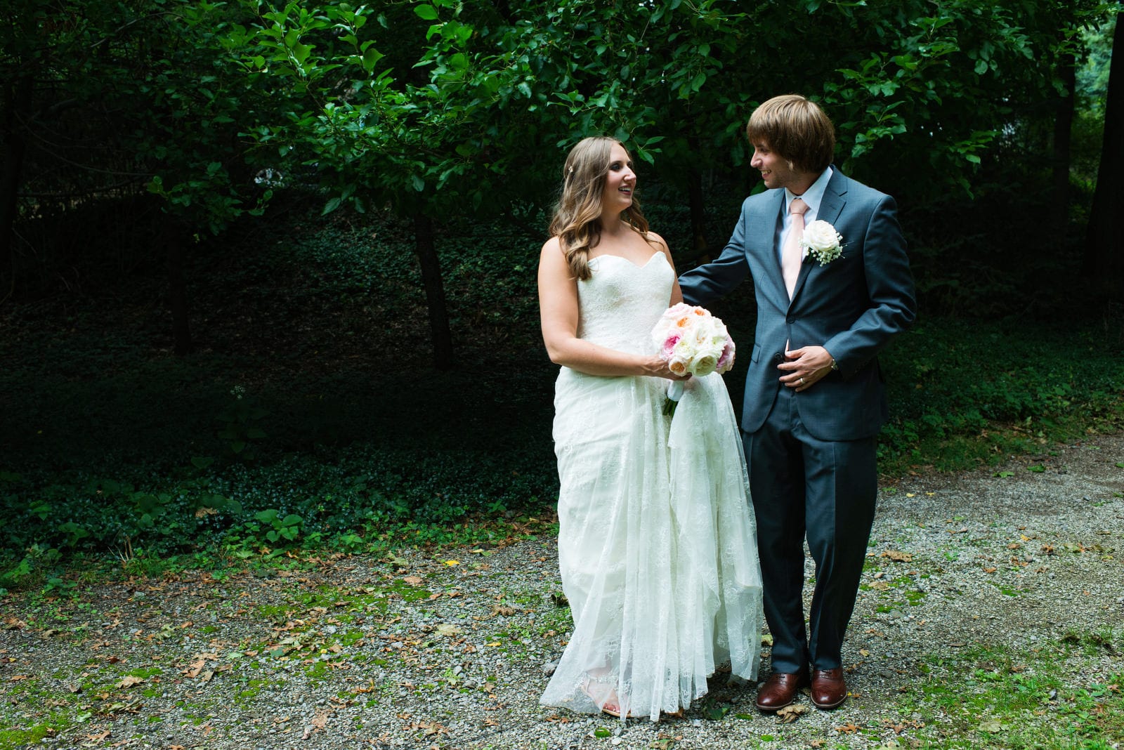 A bride and groom stand on a gravel path in the woods during their Hyeholde Wedding Pittsburgh.