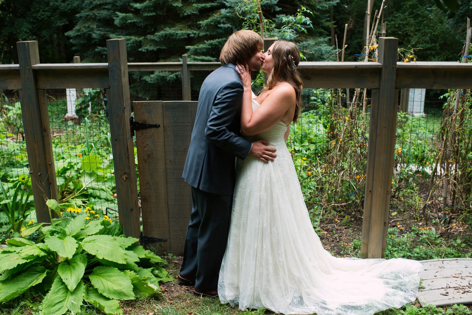 A bride and groom kiss in front of a fenced-in garden during their Hyeholde Wedding Pittsburgh.