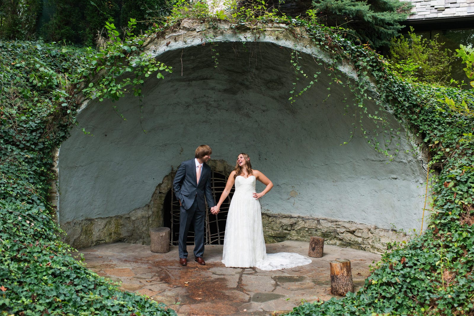 A bride and groom hold hands as they stand in an ivy covered band shell during their Hyeholde Wedding Pittsburgh.