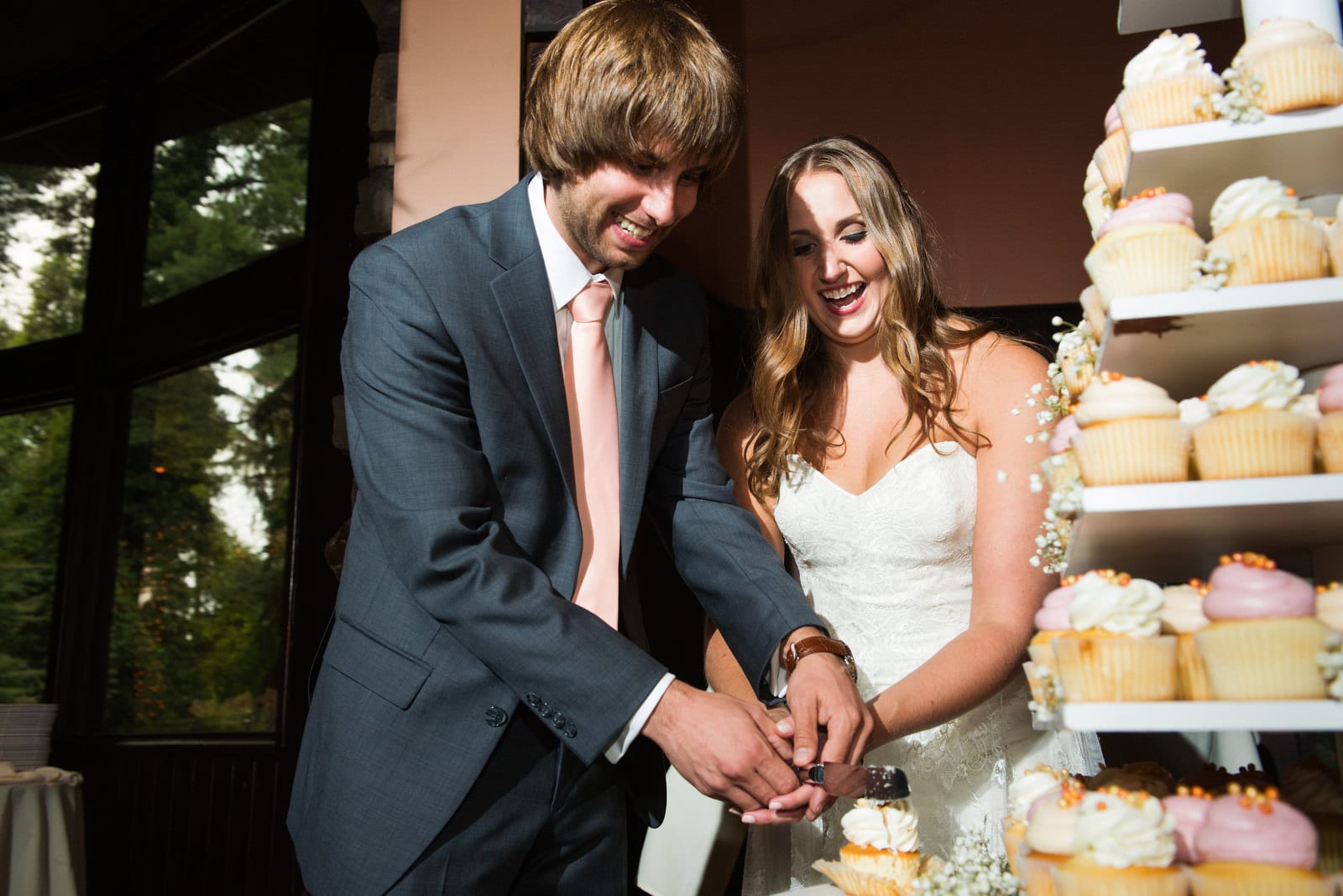 A bride and groom hold a knife while cutting a cupcake during their Hyeholde Wedding Pittsburgh.