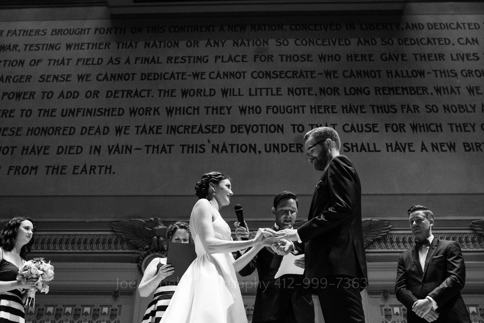 A bride slides a wedding band on the finger of her husband beneath the words of the Gettysburg Address during Soldiers and Sailors Wedding Photos.