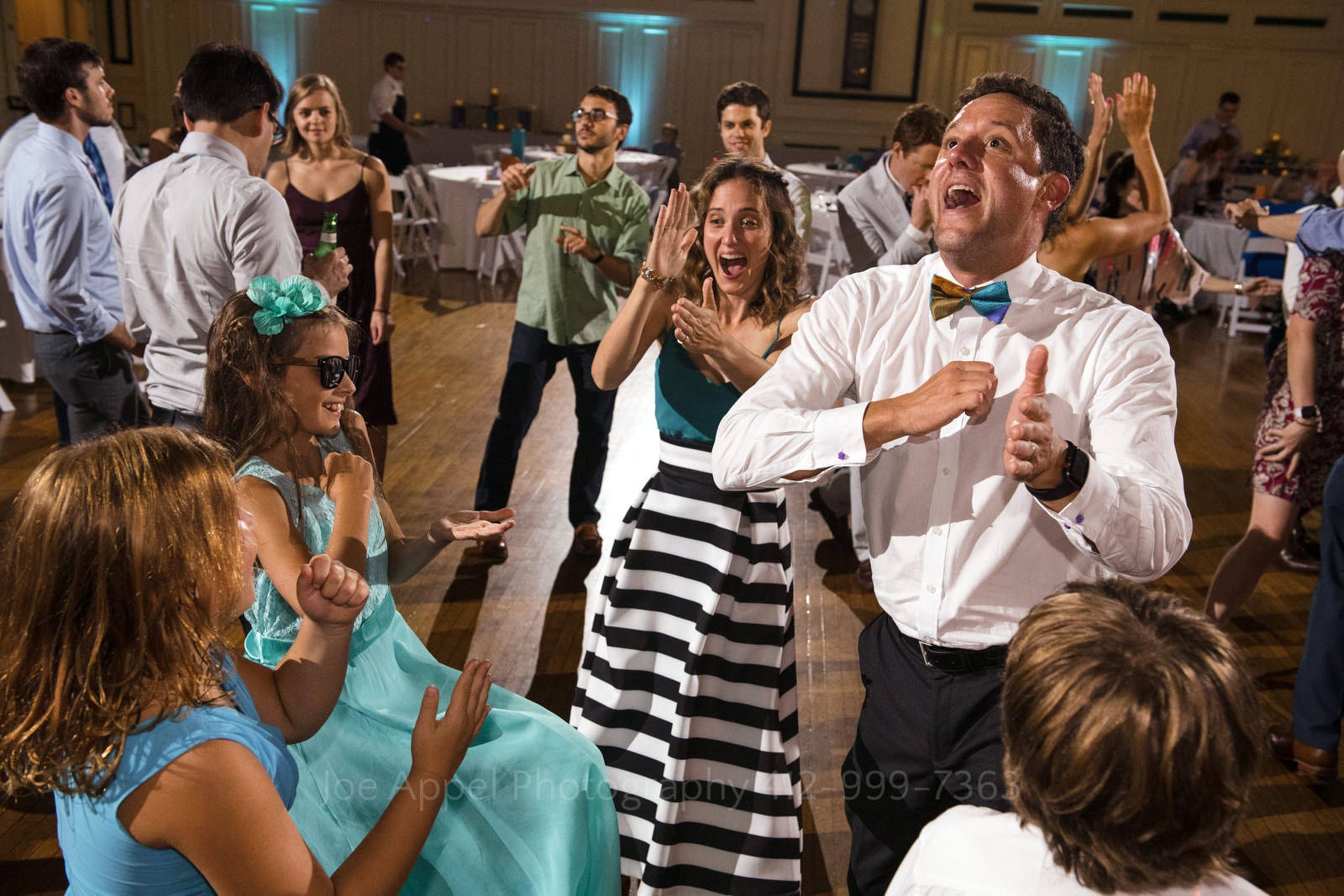A man in a white shirt and a bow tie dances with young girls in blue dresses during a Soldiers and Sailors Wedding Photos.