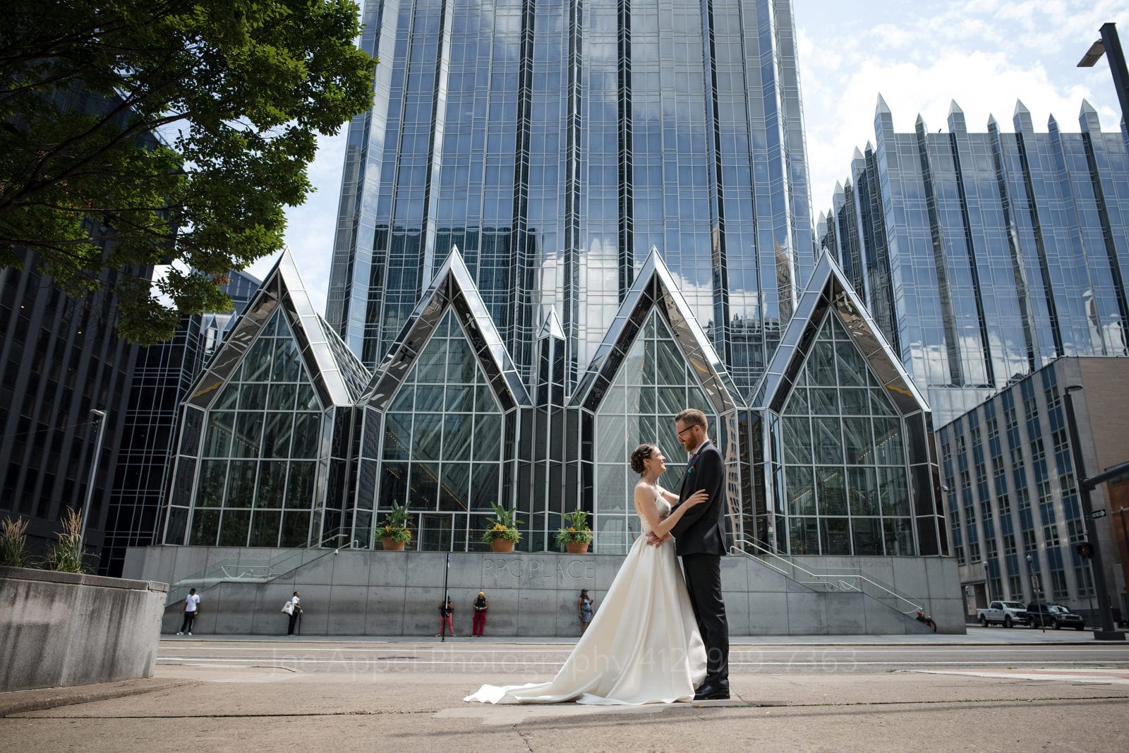 A bride and groom embrace on the street in front of PPG Place in downtown Pittsburgh. The pointed mirrored glass structure provides a dramatic backdrop.