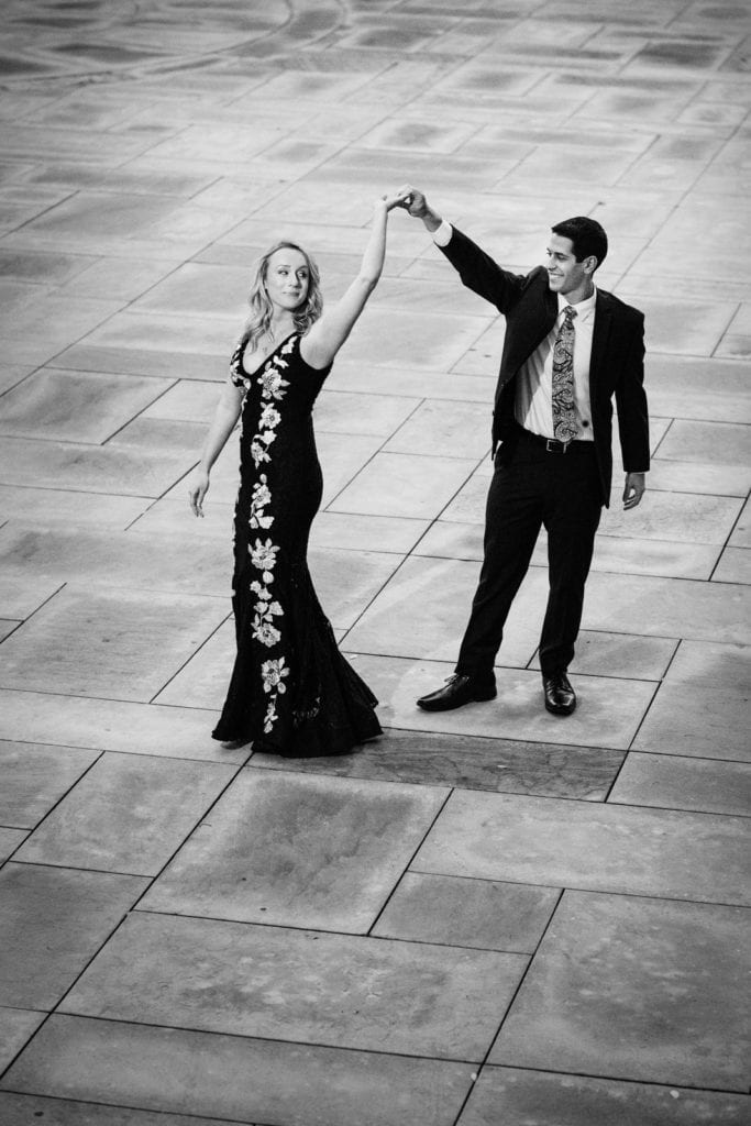 A young couple dances on a stone patio near the Cathedral of Learning while wearing formal outfits during their University of Pittsburgh engagement portraits session.
