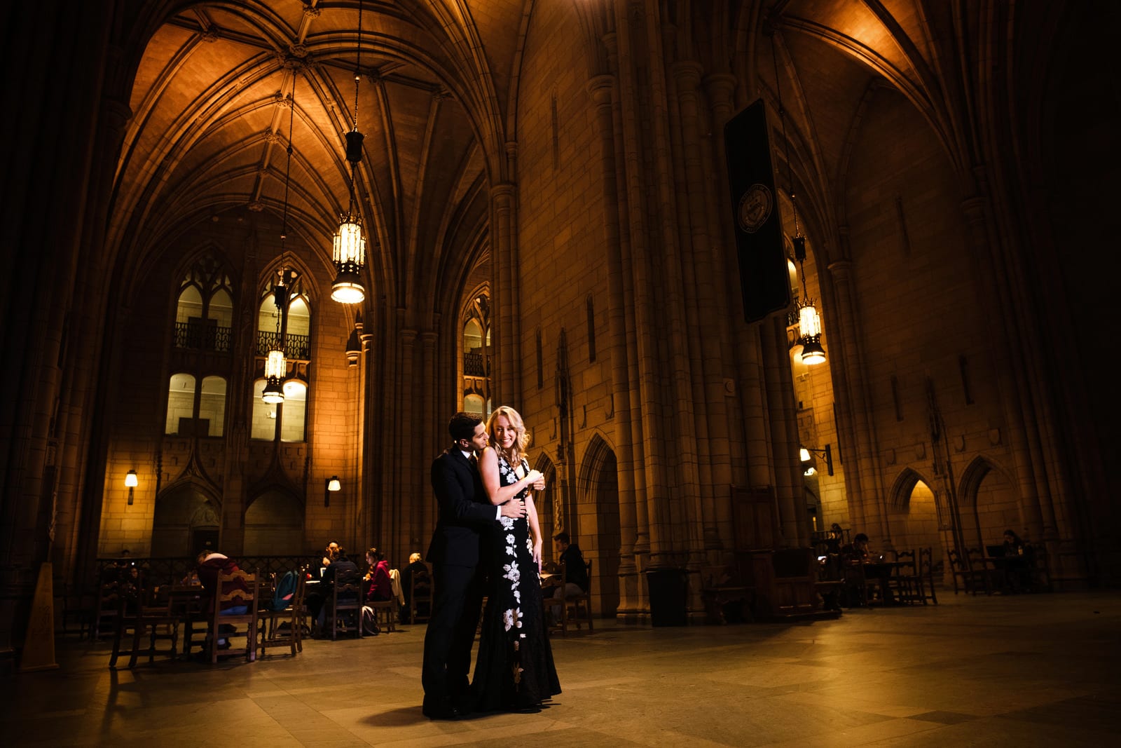 A couple embraces in the grand hall of the Cathedral of Learning during their University of Pittsburgh Engagement Portraits session.