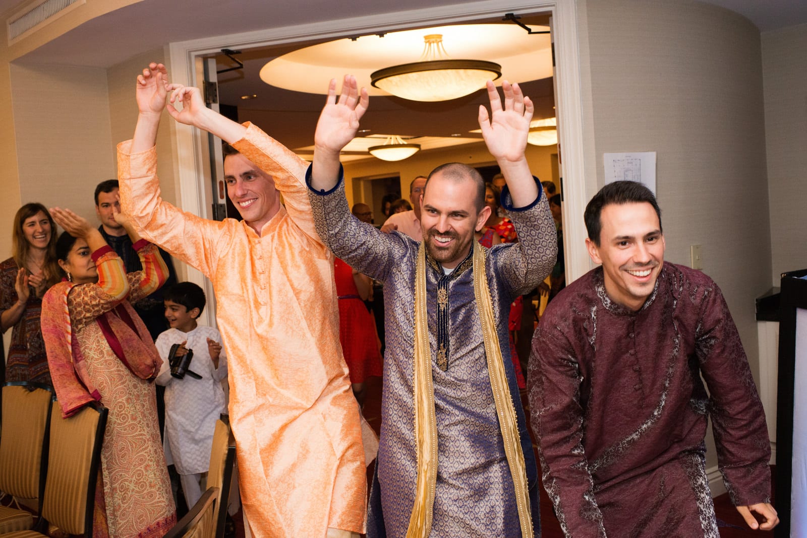 A groom enters the room for his sangeet with his brothers as they raise their hands in the air during a Renaissance Phipps South Asian Wedding.