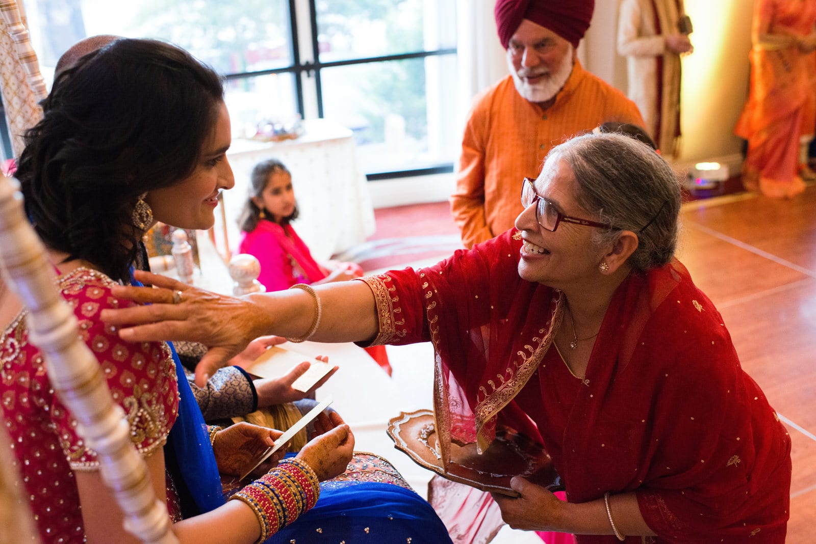 An elderly woman reaches out to bless the bride during her sangeet while a turbaned older man waits his turn behind during a Renaissance Phipps South Asian Wedding.