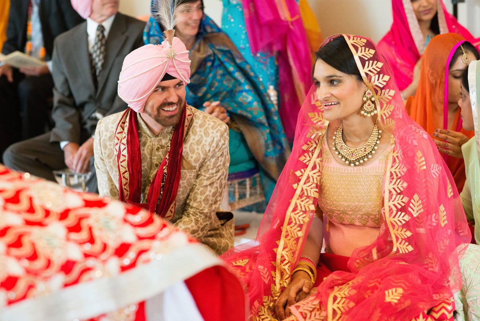 A groom in a pink turban smiles at his bride who is wearing a gold and chartreuse sari during their Sikh wedding at their Renaissance Phipps South Asian Wedding.